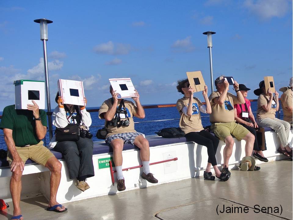 A line of people with boxes & cardboard and welder's glass view the eclipse.